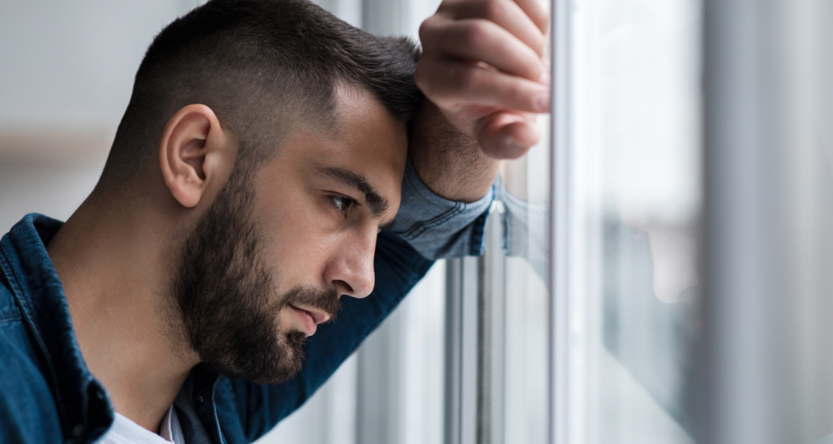 Man resting his head on his arm and looking sad out the window